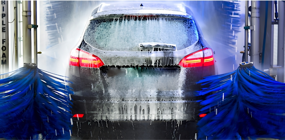 Automated car wash in progress: a sedan moving forward as blue spinning brushes rinse dirt from its sides and rear